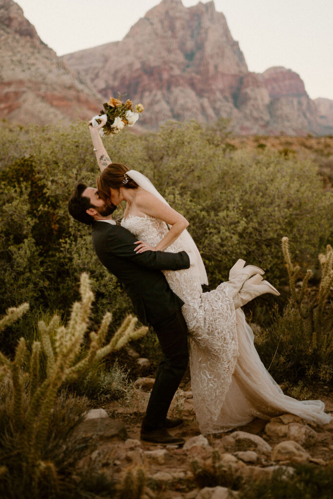 Timeless Red Rock Canyon Wedding groom lifting his bride in a kiss. The bride kicks out her feet showing off adorable boots hiding under her wedding dress. 
