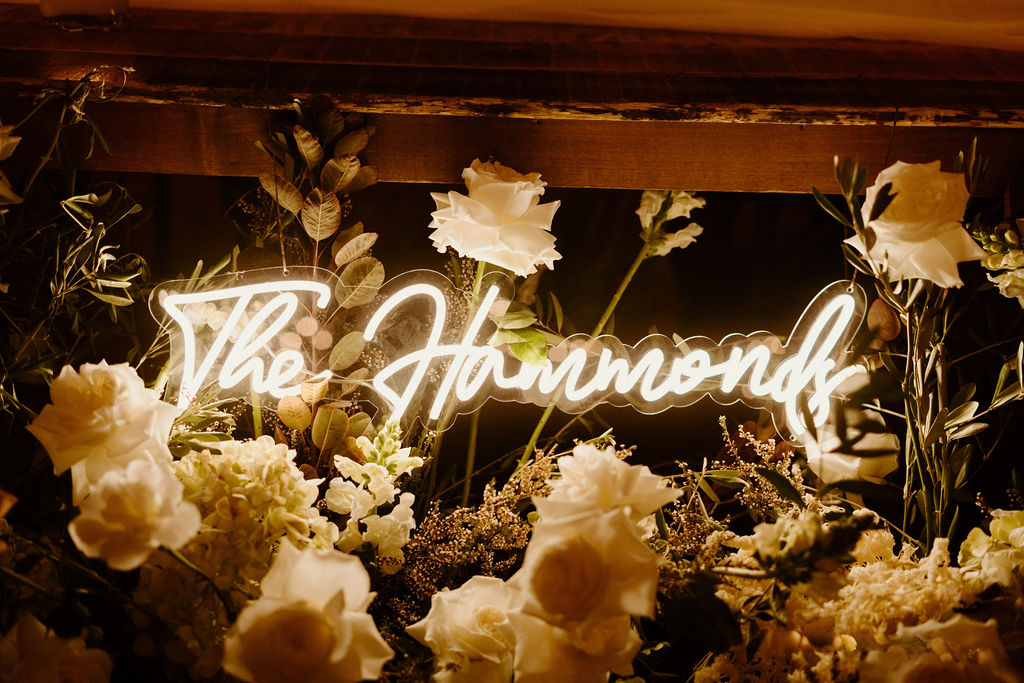 Close up of the bride and grooms light up sign on at night wrapped in the ground floral arch. 