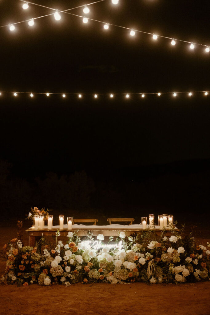 His and her table at night. With lights illuminating above, candles on the table, and a light up sign with the bride and grooms last name lit up. 