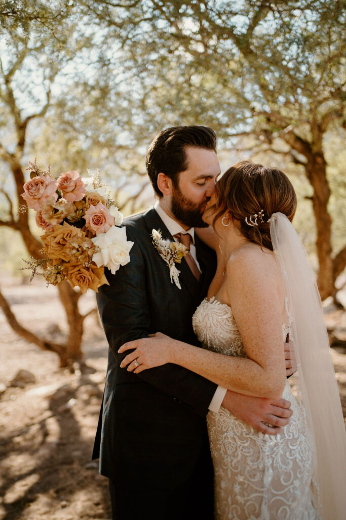 Bride and groom kissing as she holds her bouquet wrapped around the grooms shoulders. 