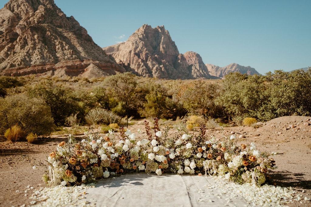 Timeless Red Rock Canyon Wedding with a close up perspective of the ground floral arch with white and toffee colored roses. 