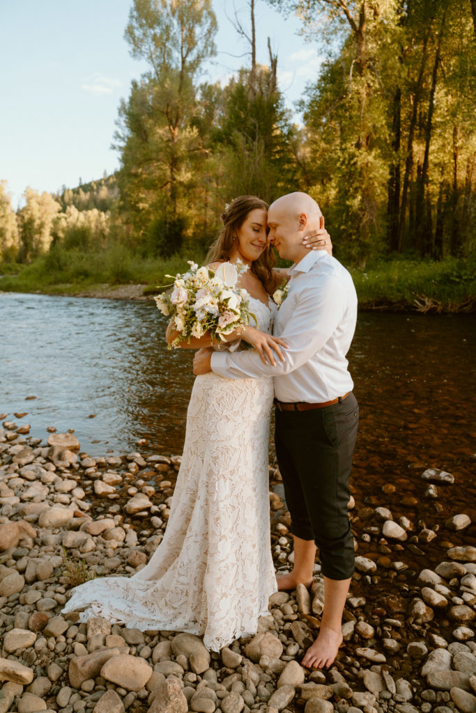 What is a Natural & Organic Styled Wedding. Newlyweds stand on the cobble stones on the side of the lake at steamboat 