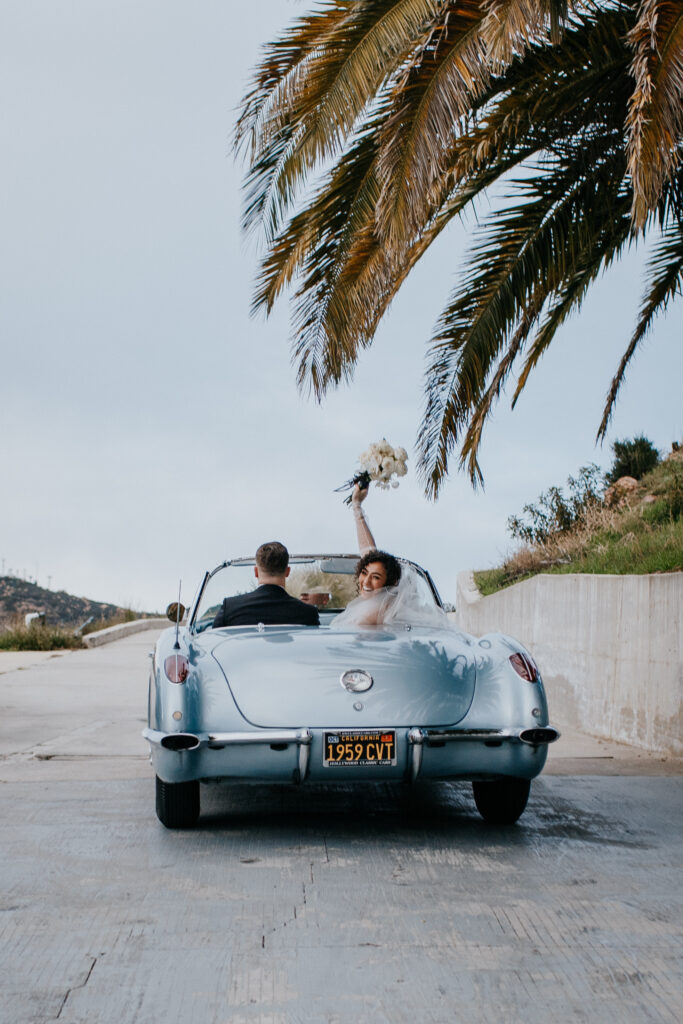 Bride and groom leaving in blue classic getaway car 