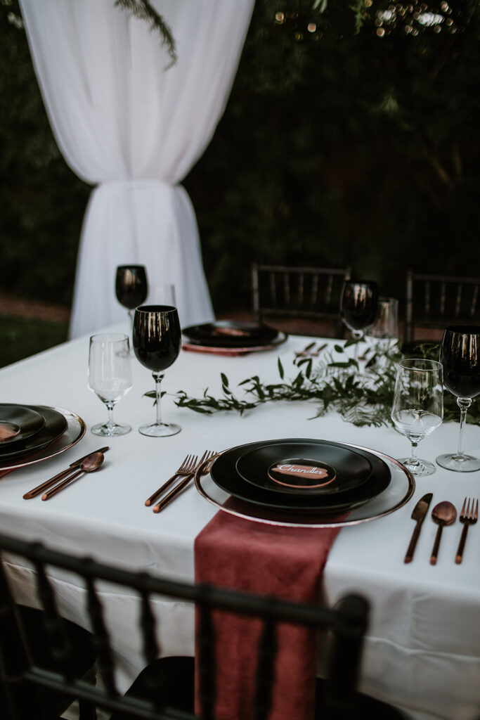 Dark and Moody table decor.  Black plates and wine glasses. Burgundy silverware and napkins