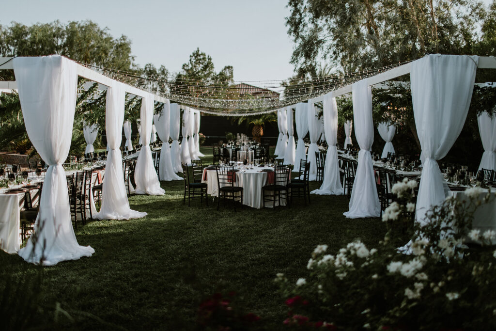 Wide view of a wedding set up. White draping with tables lining both sides. Sting bistro lights above, and tables down the center. 