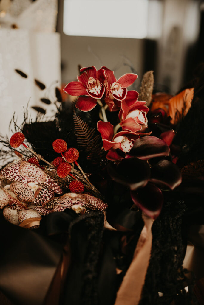 Close up of a dark and moody bouquet. With leopard print and bright red flowers mixed in with black floral pieces. 
