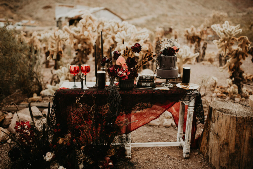 A dark and moody wedding table decoration. Black and shades of red. On the ground is floral decorations with different types of textures. 
