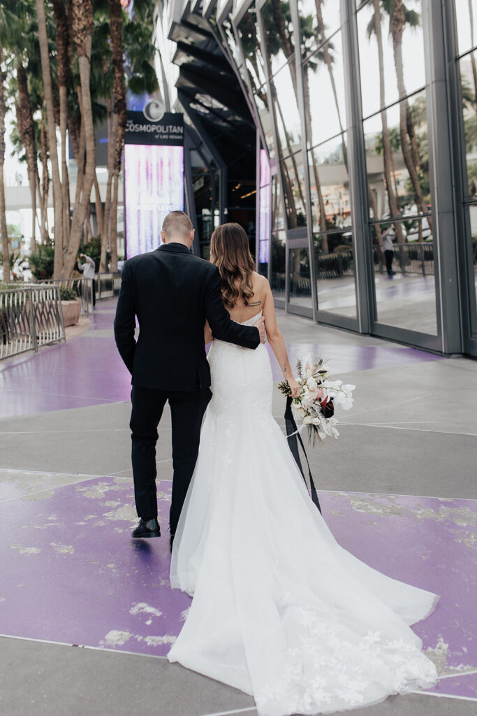Bride and groom walk along a pathway at the Cosmopolitan. The walkway has bright purple designs along the path floor. The brides train flows behind her.