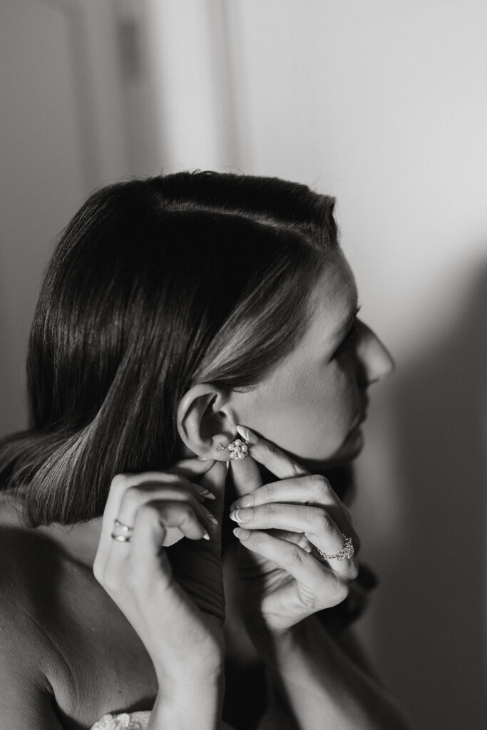 Black and white photo of bride putting on her earing. 