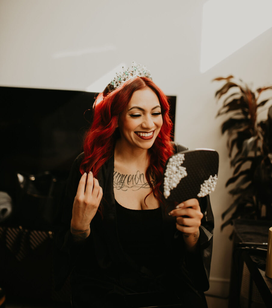 Gorgoues bright red haired bride looking at her finished reflection with a crown as her wedding accessory 