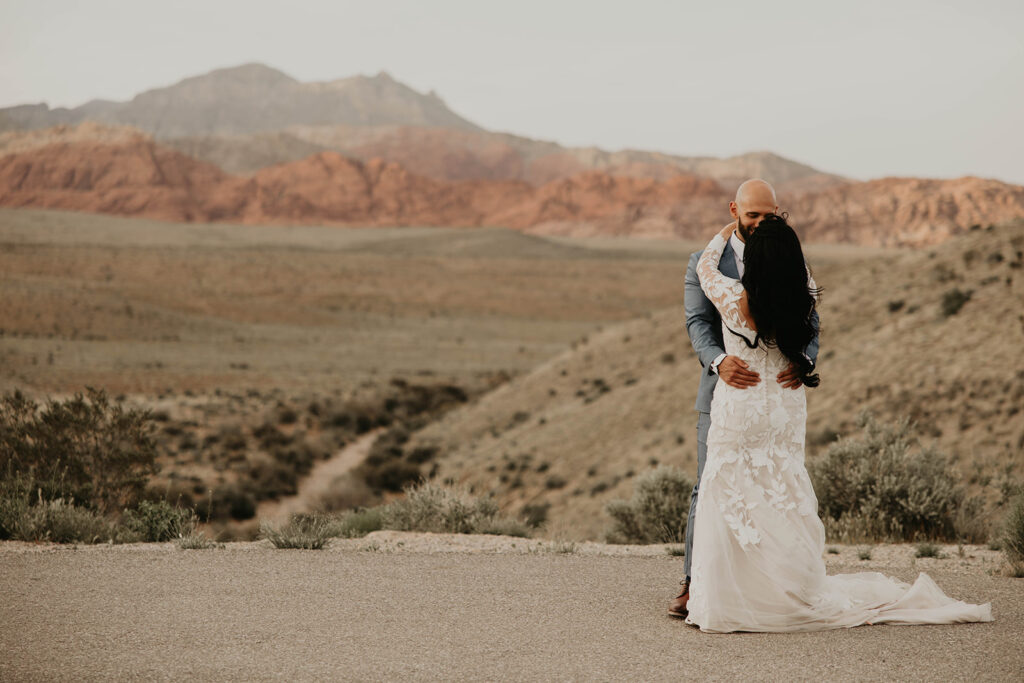 Just The Two Of Us Elopement in the Desert Bride with her long brunette hair and floral lace mermaid dress dances with her groom in the Red Rock Canyon 
