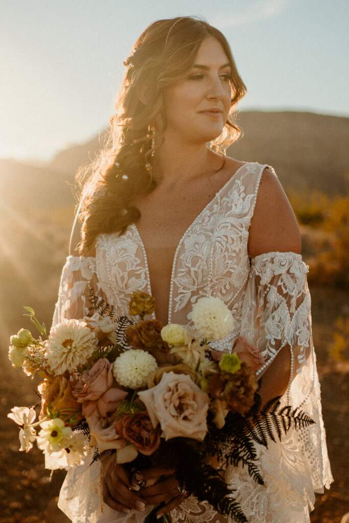 Close up of bride holding her boho styled bouquet. She wears a a deep V-neck boho styled dress with slip on sleeves on her arms. 