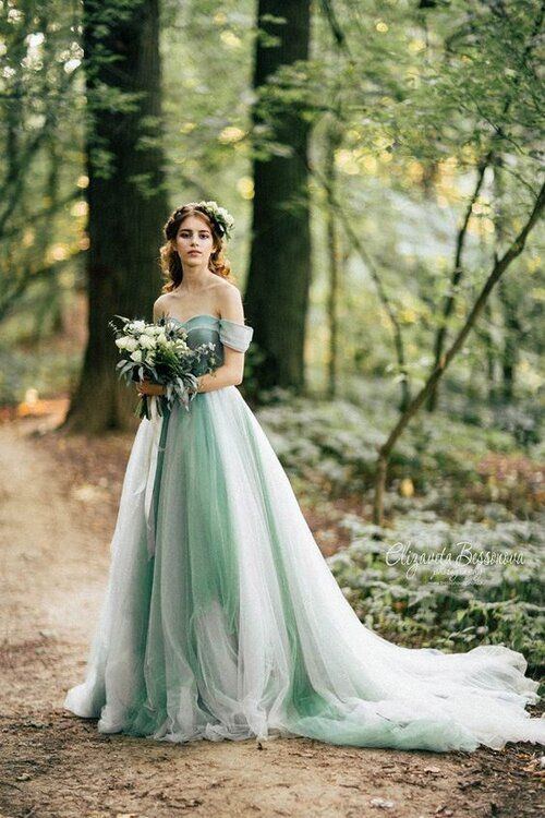 The Ultimate Guide to Different Types of Wedding Dresses: From Classic to Contemporary. Rich green and white sweetheart wedding dress with off the shoulder sleeves. The bride stands in the forest on a path holding her bridal bouquet. 