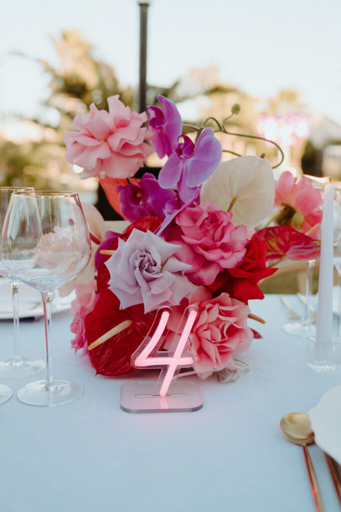 Close up of a pink, purple, white, and red floral center piece. With a LED Pink table number. 