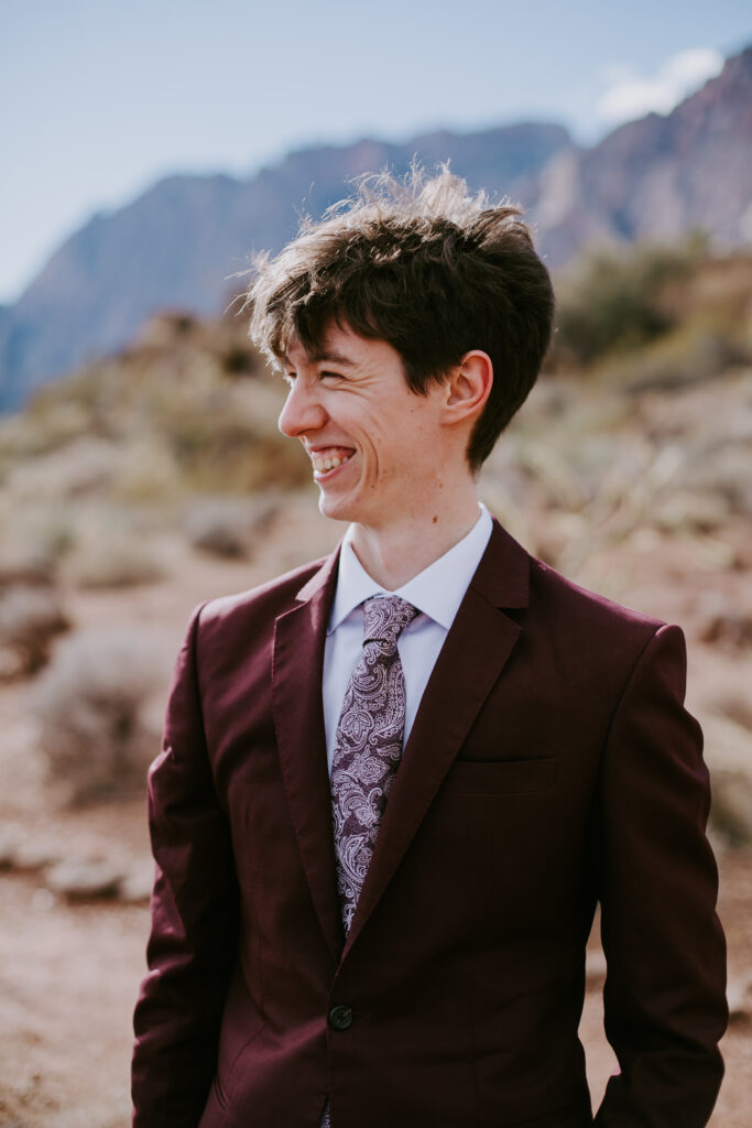 Love Unleashed: Colorful Las Vegas Elopement. The groom wears a deep maroon suit with purple paisley tie. He smiles widely as he becomes the focus of the photo. 