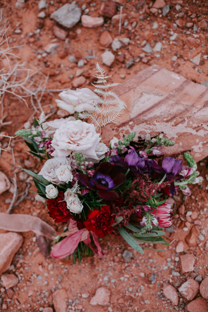 Love Unleashed: Colorful Las Vegas Elopement. Pink, red, purple, and maroon bridal bouquet lays on the red desert sand. 