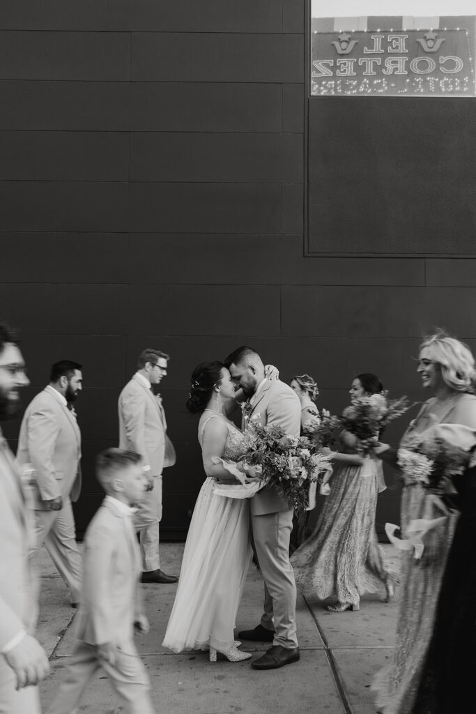 Fun & Creative Wedding Day Photo Poses and Ideas Bride and groom hold each other as their wedding party walks through the black and white photo. Creating a moving effect around the couple. 