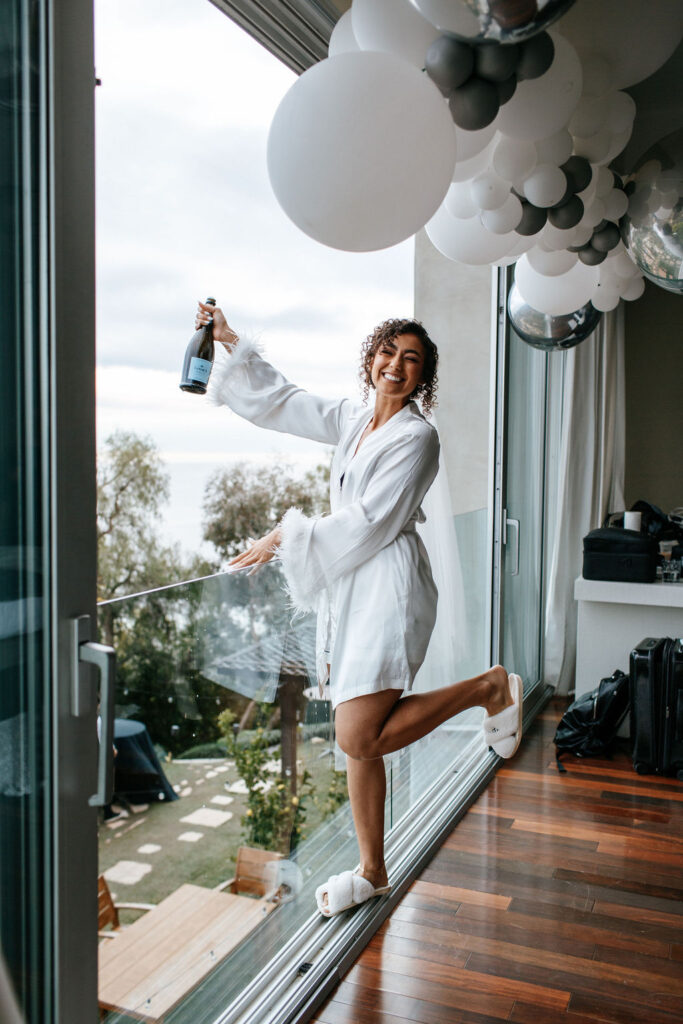 Unleash the Magic: Why Your First Look Should Steal the Show. Bride doing champagne spray while getting ready 