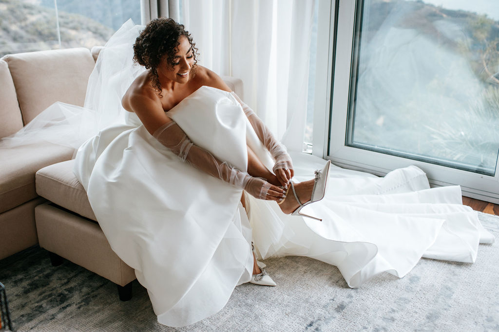 Unleash the Magic: Why Your First Look Should Steal the Show. Bride smiling putting on shoes while getting ready for first look.