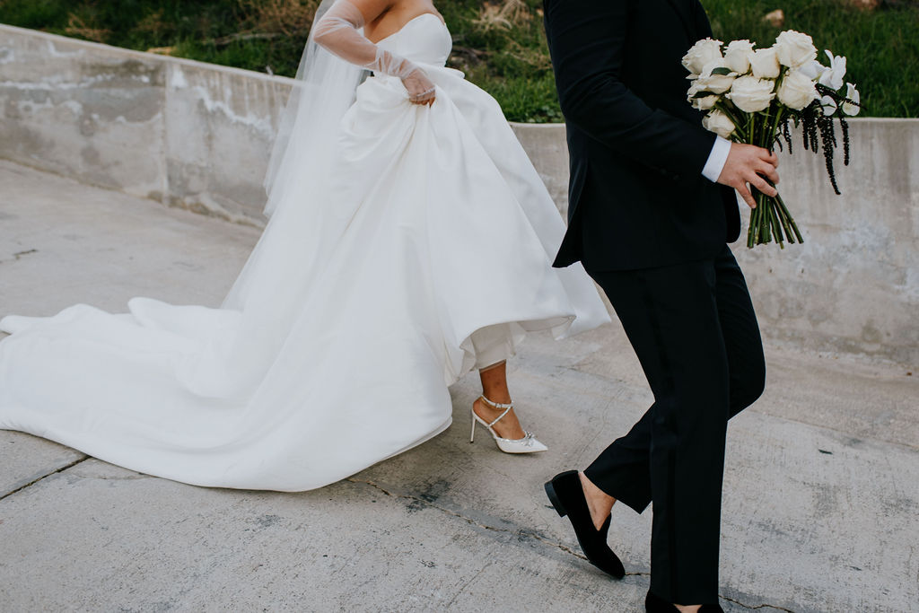 Unleash the Magic: Why Your First Look Should Steal the Show. Groom holding brides bouquet while bride holds dress up walking down the hill 