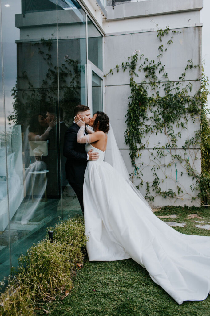 Unleash the Magic: Why Your First Look Should Steal the Show. Bride and groom kissing against glass window 