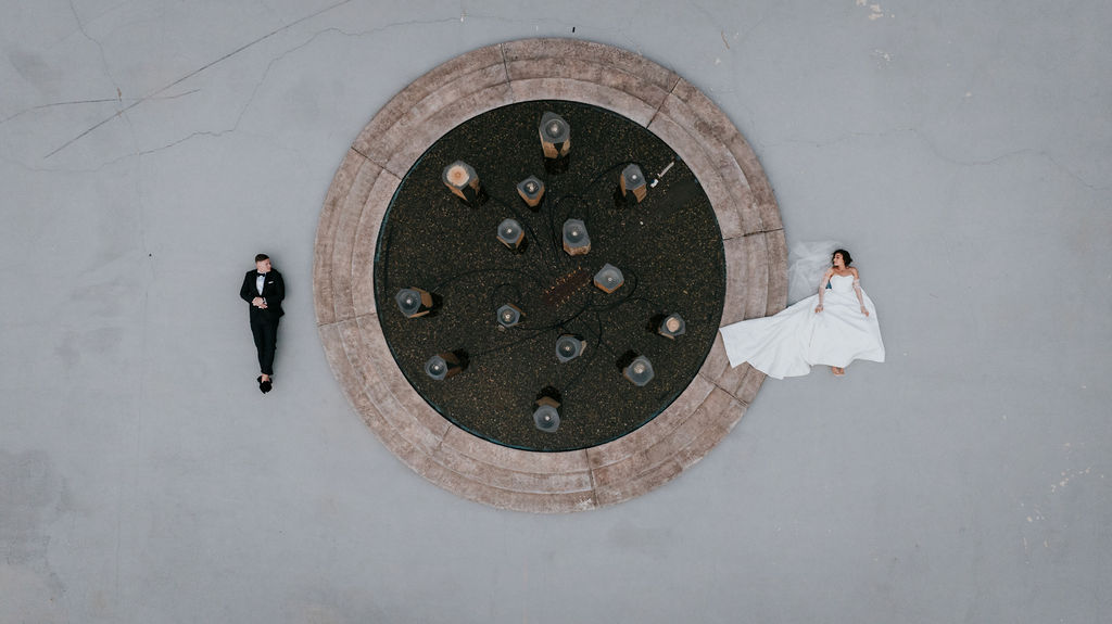 Overhead shot of Bride and groom laying on either side of the rock fountain 
