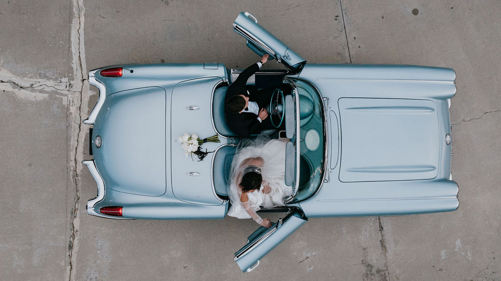 Bride and groom getting in classic blue car 
