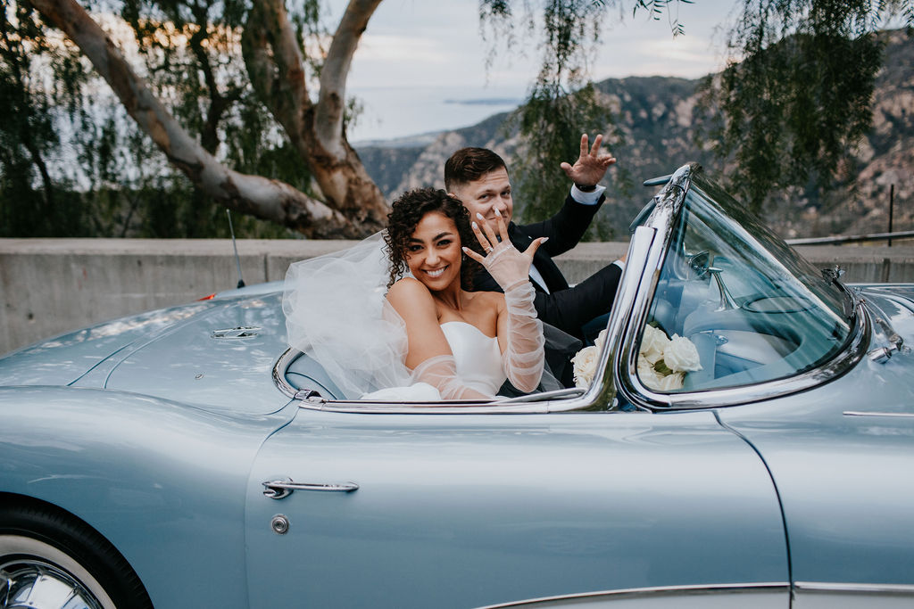 Bride showing off ring while driving off in vintage blue car after getting married. Unleash the Magic: Why Your First Look Should Steal the Show