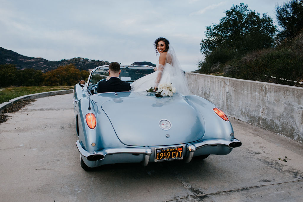 Unleash the Magic: Why Your First Look Should Steal the Show. Bride sitting on back of classic  blue car 