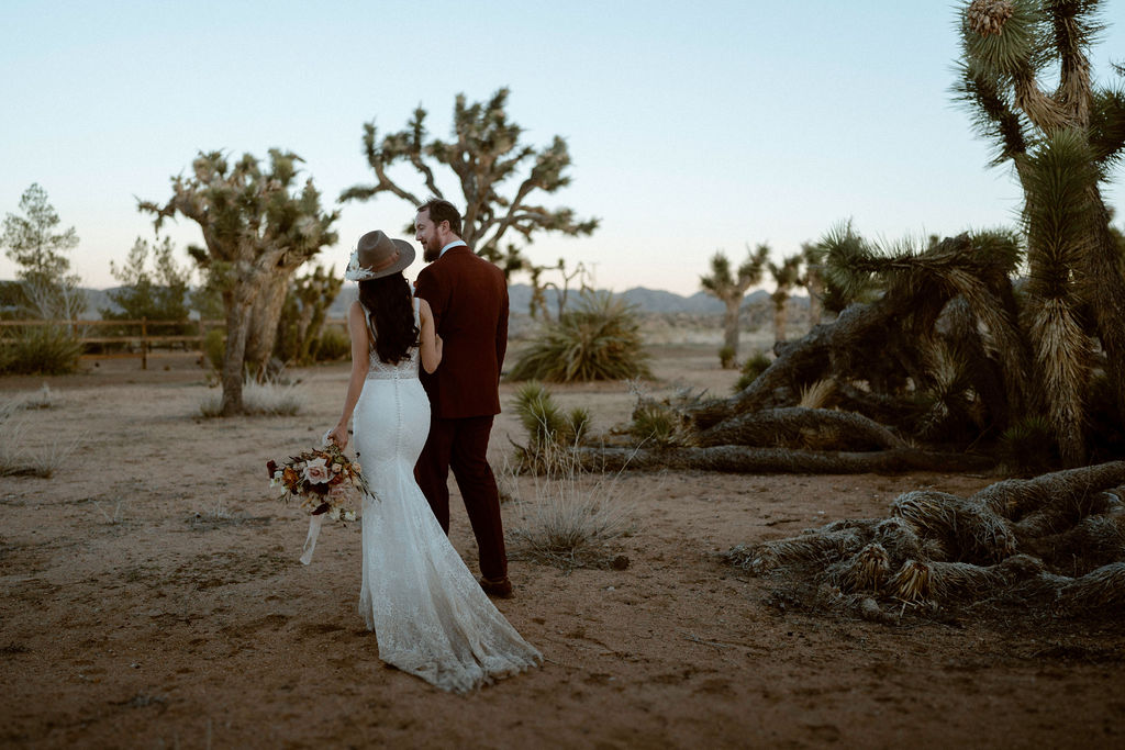 Bride with hat walking with groom with Joshua Tree's 