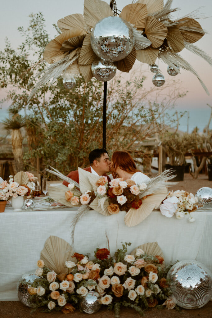 Newlyweds kissing at sweetheart table with hanging installation 