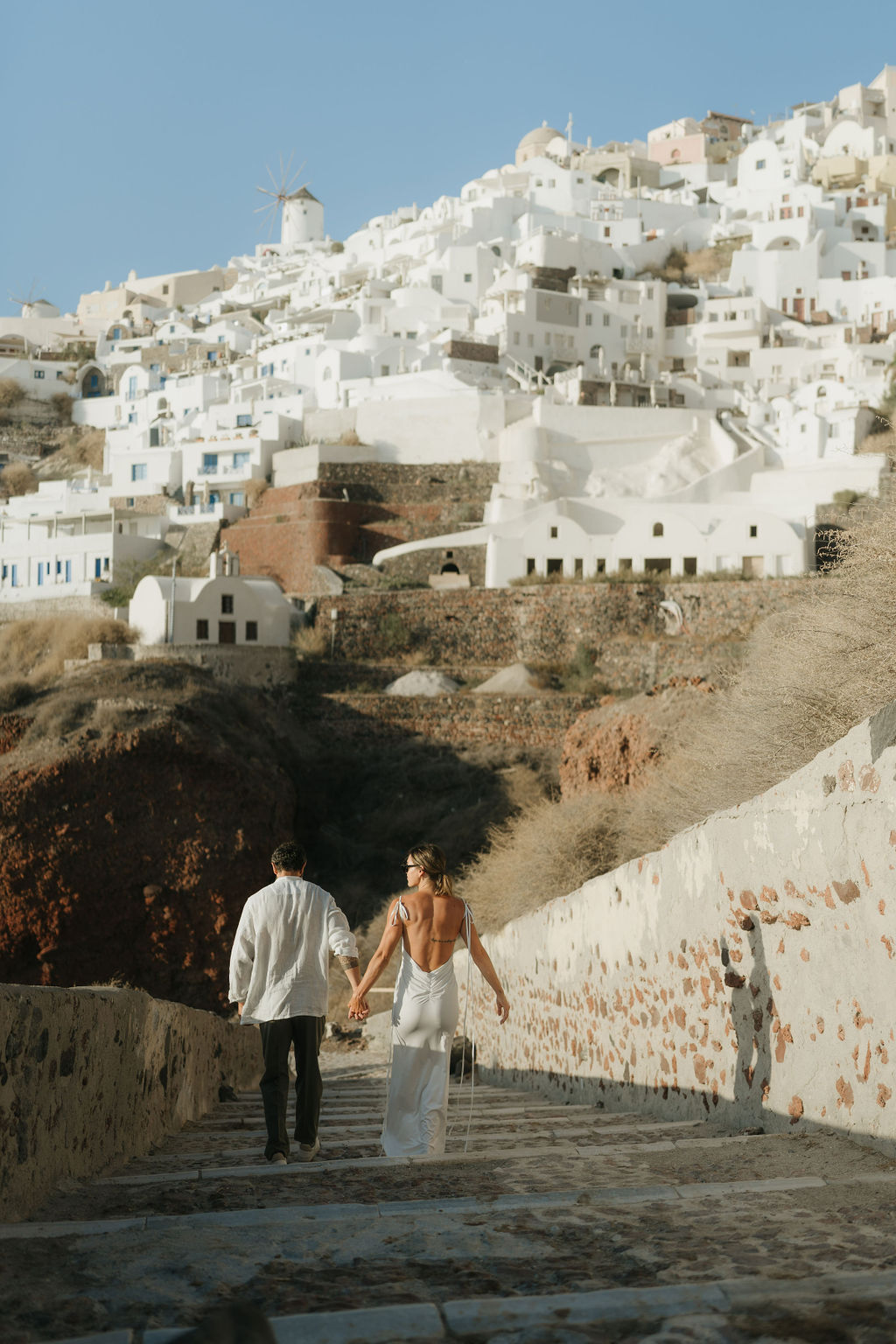 A couple embraces joyfully on a stone path with the backdrop of Santorini 