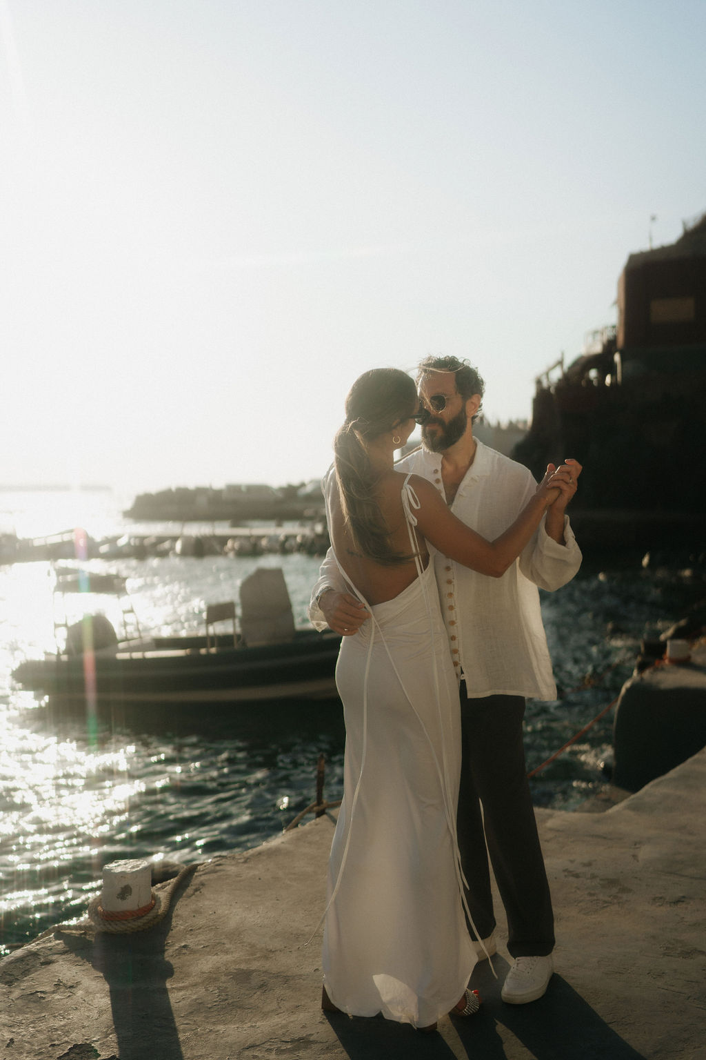 A couple dancing along a seaside, with the woman wearing a white dress and the man in a white shirt 