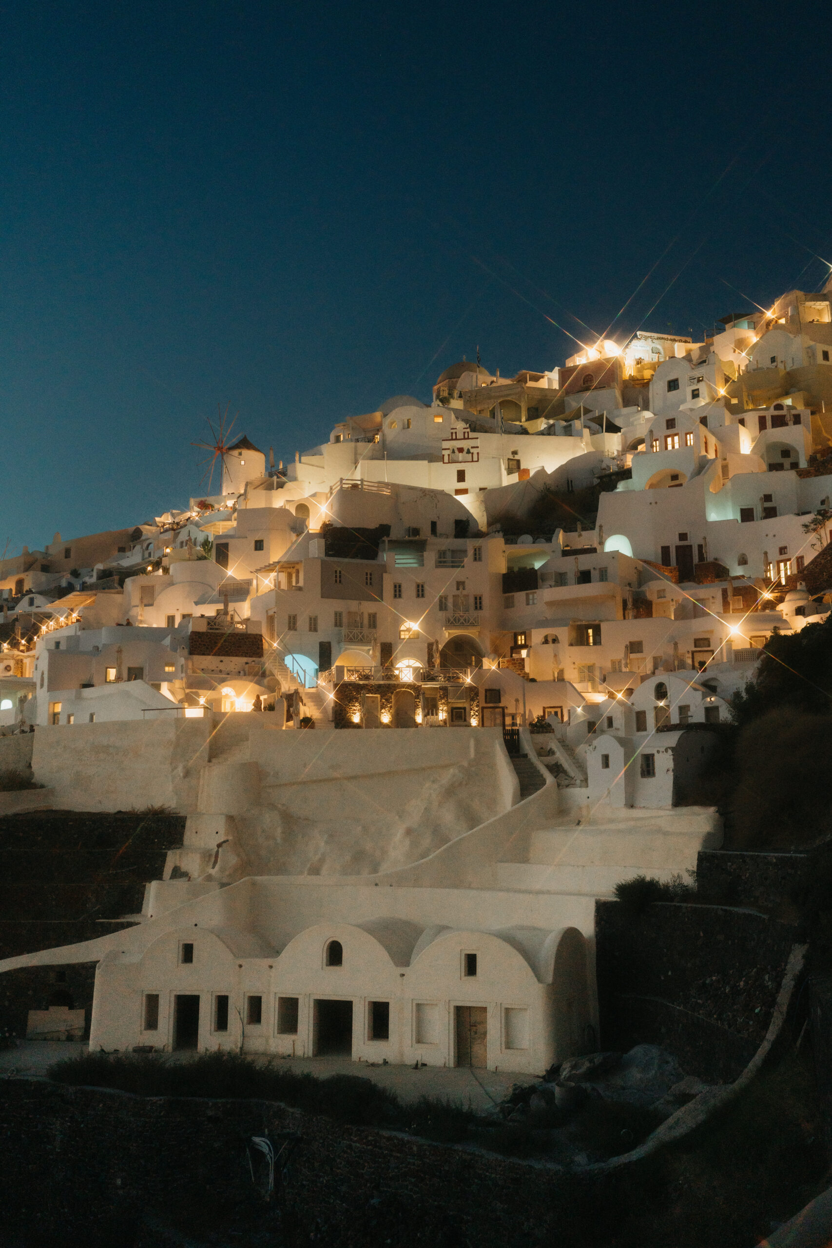 Twilight view of the whitewashed buildings of santorini, greece, with illuminated windows and winding stairs.