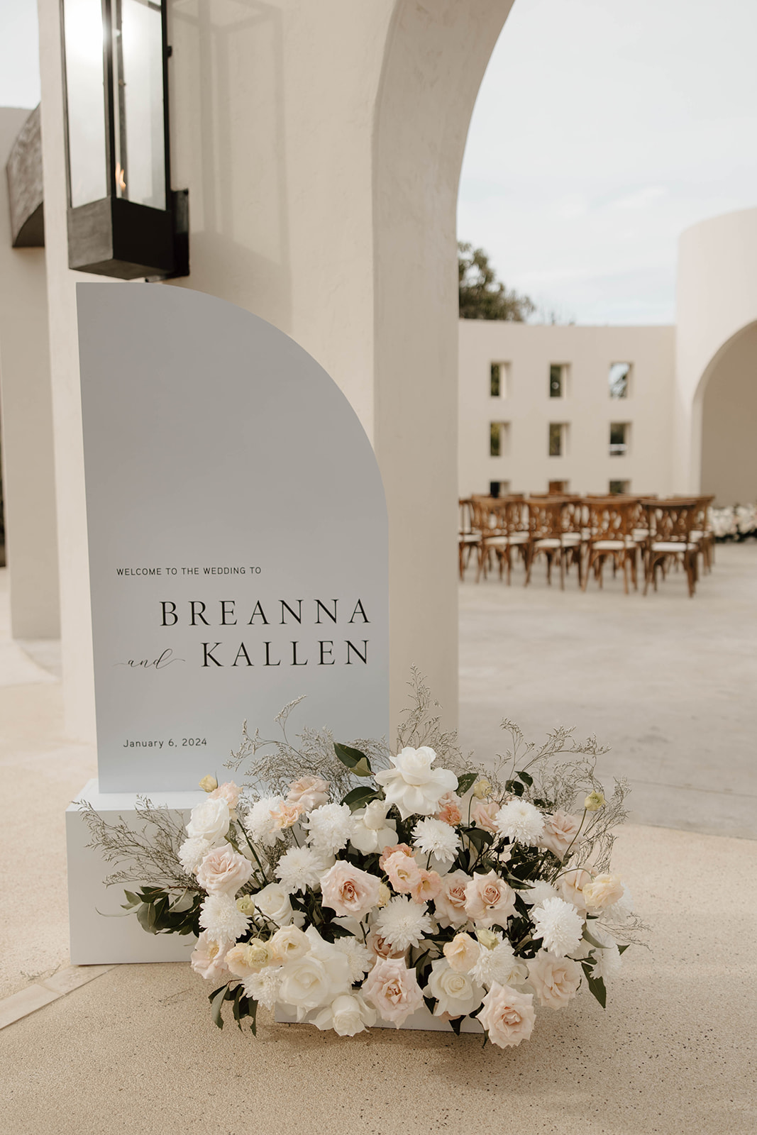 Wedding welcome sign featuring the names "breanna and kallen" with a date, placed beside a floral arrangement.