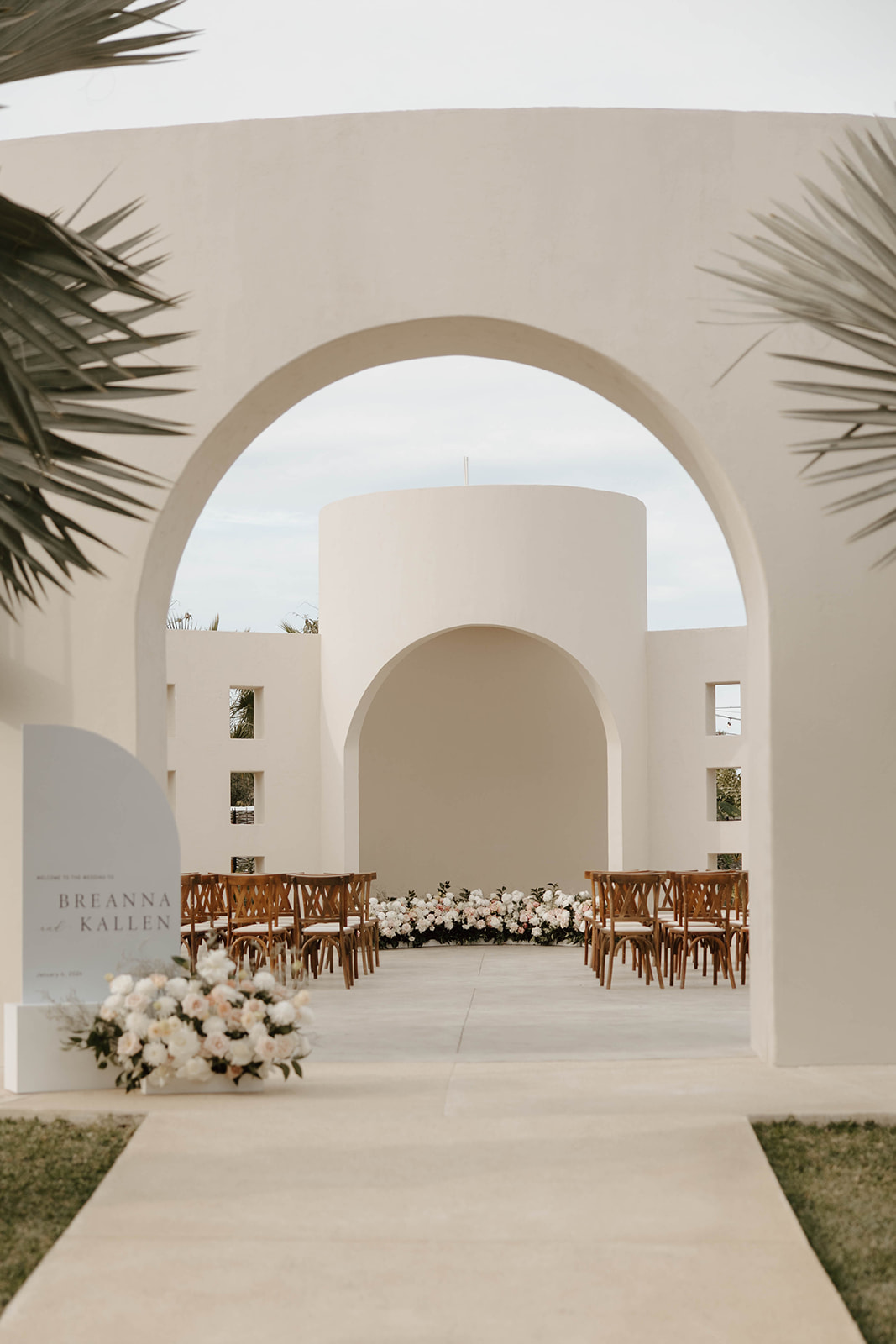 An outdoor wedding venue featuring a geometric archway, wooden chairs, and floral decorations along a central aisle at Baja Luna venue 