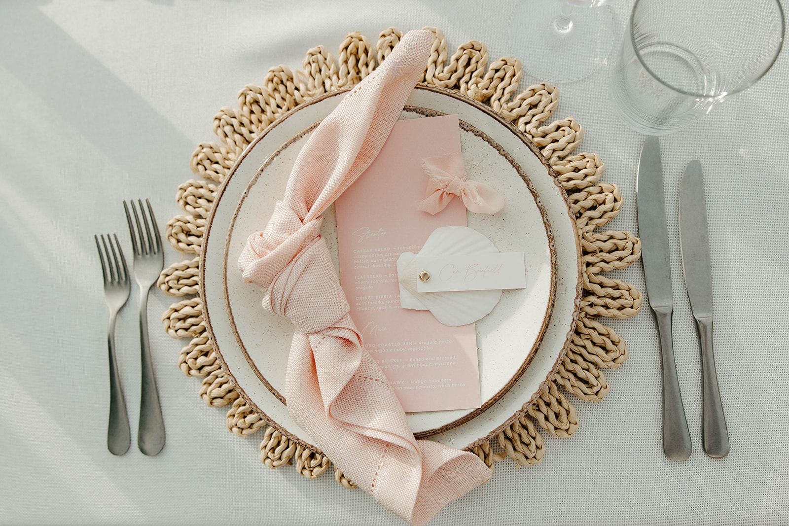 Elegant table setting with a pink napkin, menu, and place card on a ceramic plate for a Cabo San Lucas Wedding