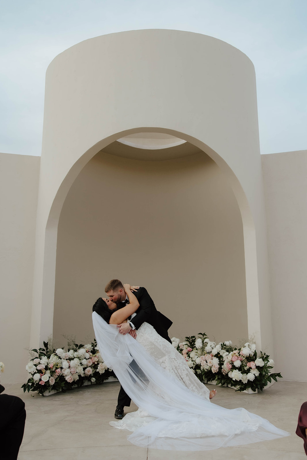 Bride and groom sharing their first kiss beneath an archway with floral decorations at a Cabo San Lucas wedding