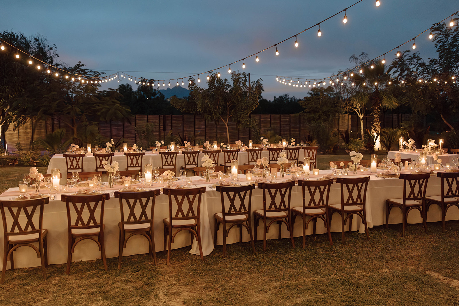 An elegantly set outdoor dining table with a white tablecloth and floral decorations under string lights at a Cabo San Lucas wedding