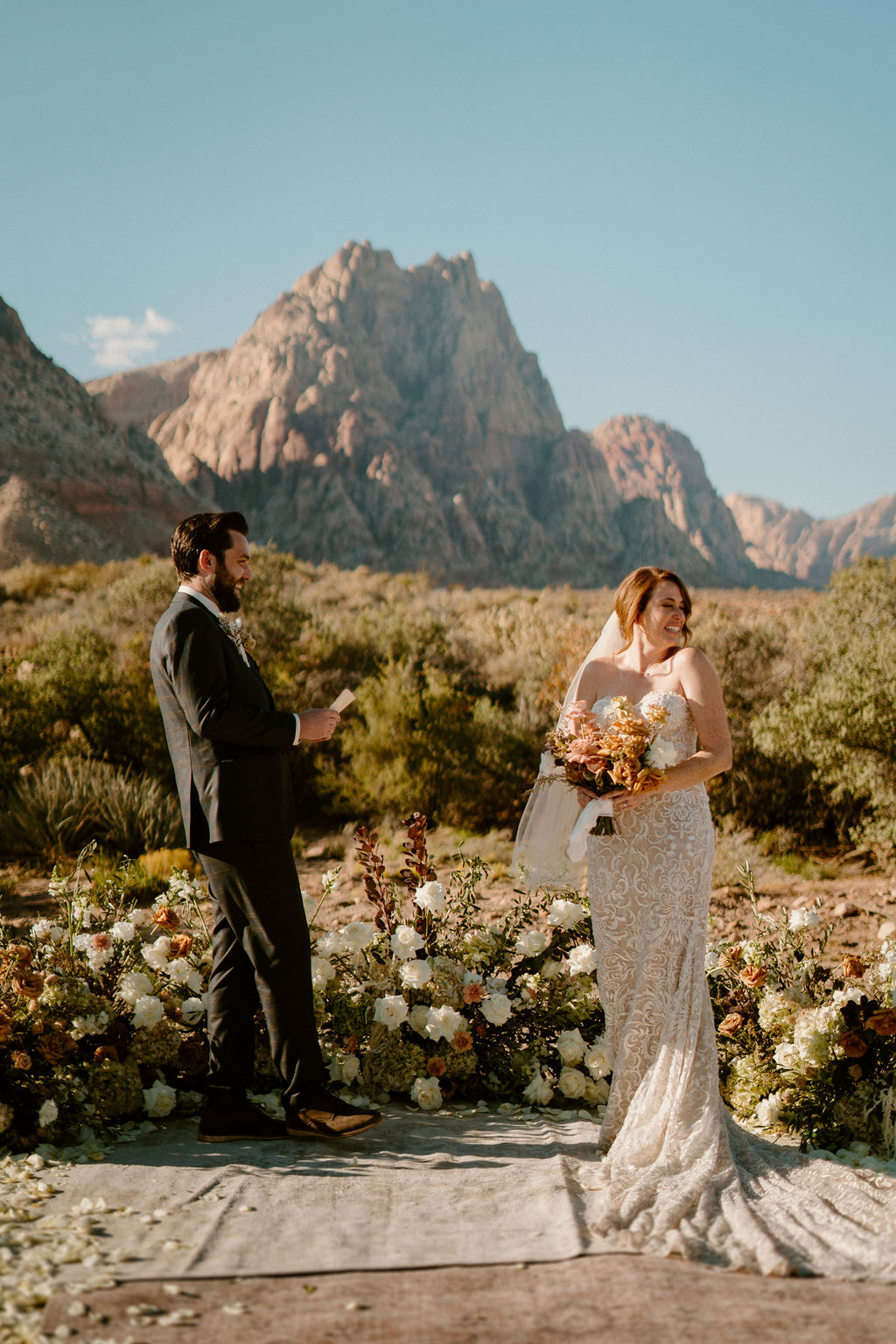 A wedding ceremony taking place outdoors, with a couple and officiant standing amid floral arrangements in a desert setting with a rugged mountain backdrop at Red Rock Canyon