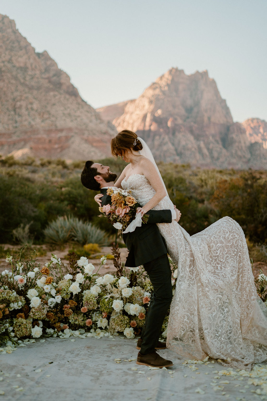 A wedding ceremony taking place outdoors, with a couple and officiant standing amid floral arrangements in a desert setting with a rugged mountain backdrop at Red Rock Canyon