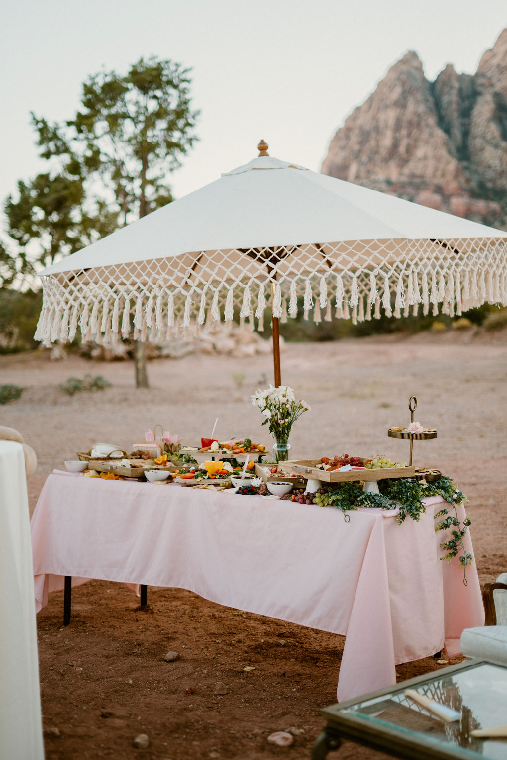 Outdoor buffet table covered with various dishes under a white umbrella, set against a backdrop of rugged mountains.