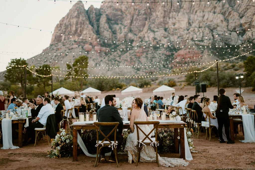 Outdoor wedding reception with guests seated at tables under string lights, set against a scenic mountain backdrop at dusk at Red Rock Canyon