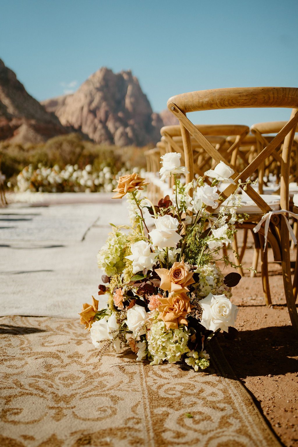 Floral wedding arch with white petals on the ground, set against a backdrop of rugged mountains and sparse desert vegetation at Red Rock Canyon