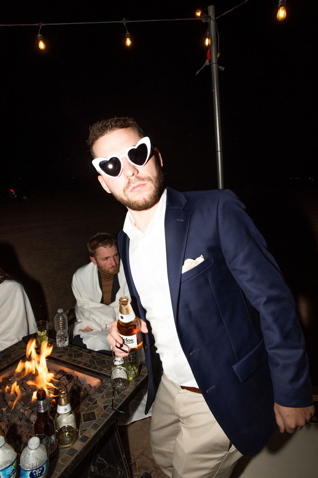 Person in sunglasses holding a beer, leaning towards the camera 
