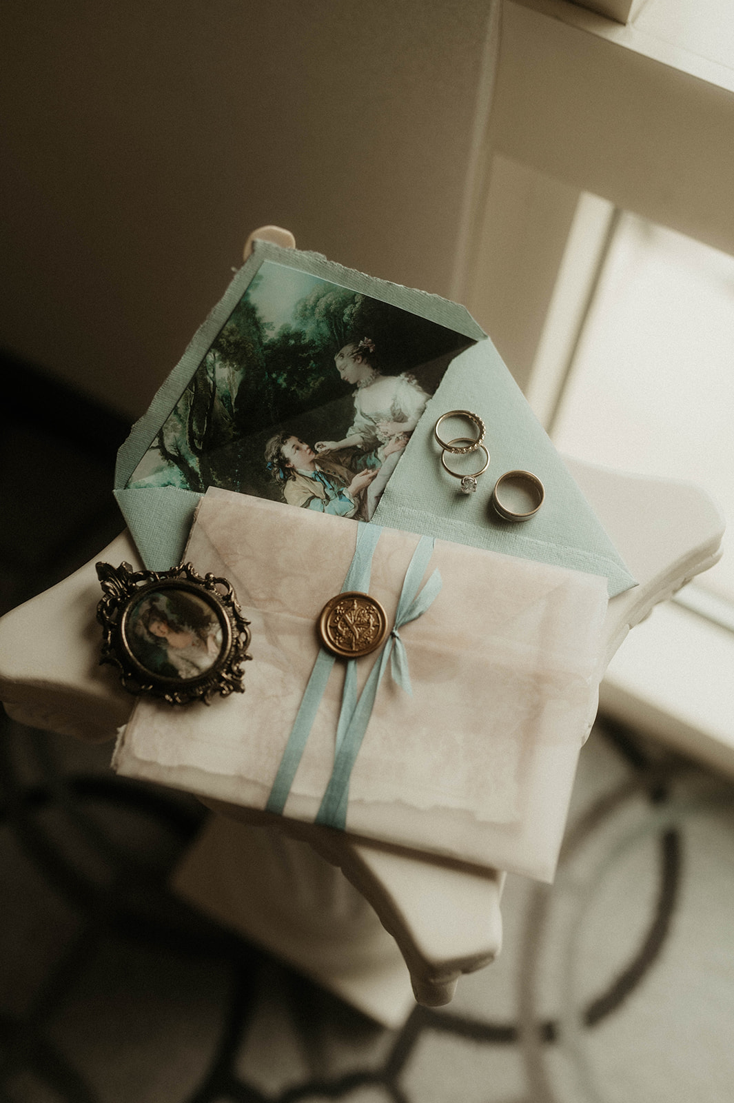 An antique-style photo featuring a stack of vintage wedding invitations, a romantic painting, a ribbon, and old jewelry on a creamy fabric background for a bridgerton wedding