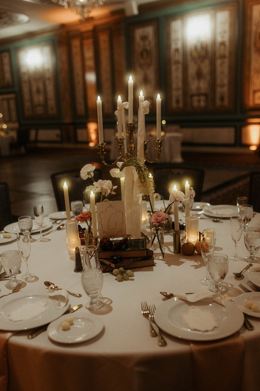 Elegant wedding reception table set for a dinner under a grand chandelier, with ornate wall panels and numerous lit candles for a bridgerton themed wedding