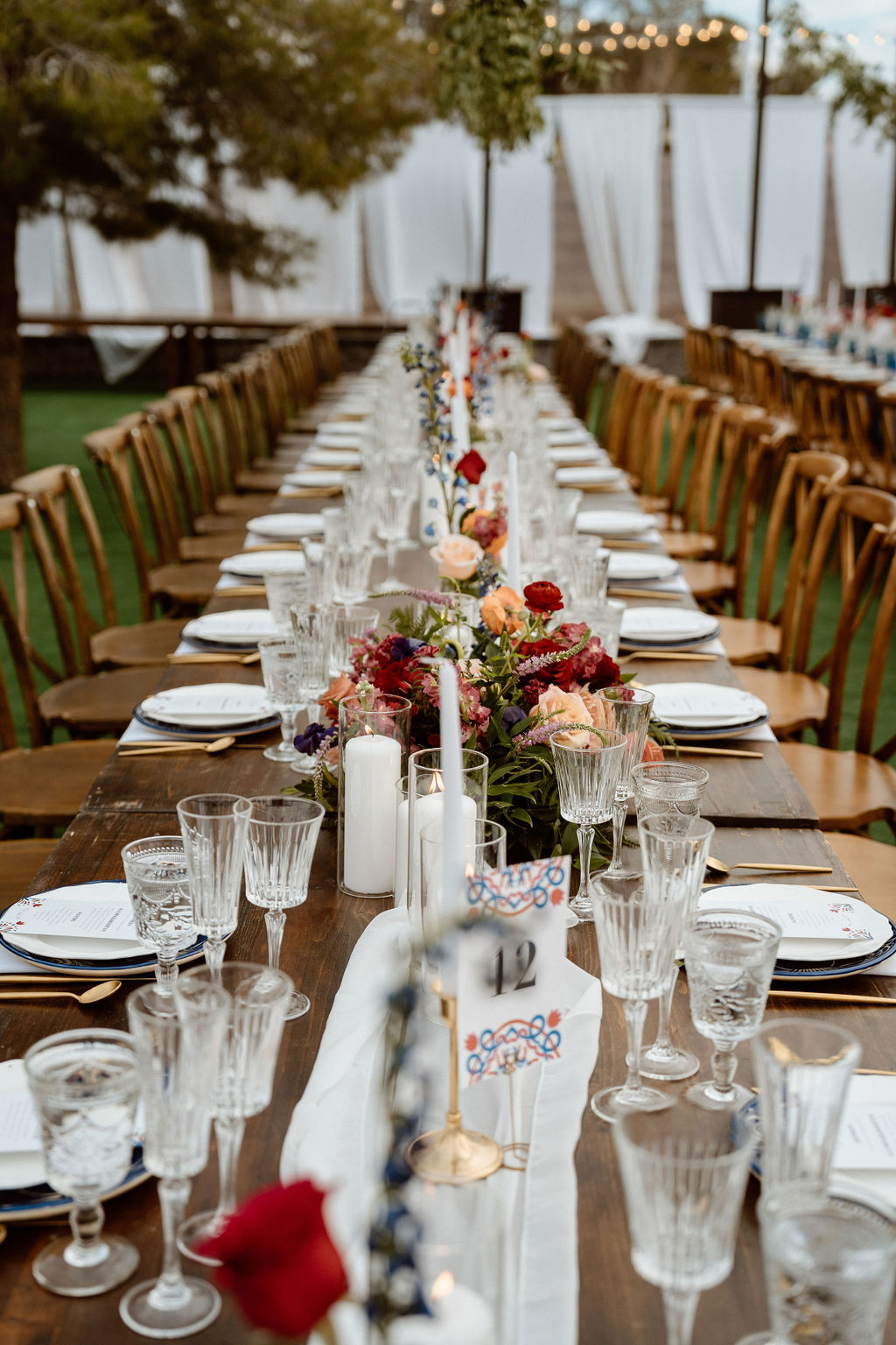 Elegantly set outdoor dining tables with wooden chairs, blue table runners, and decorative floral centerpieces for an hacienda themed wedding