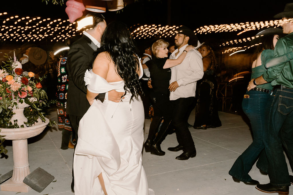A couple dances passionately at night while a live band with brass instruments performs, surrounded by decorative lights and hanging lanterns.