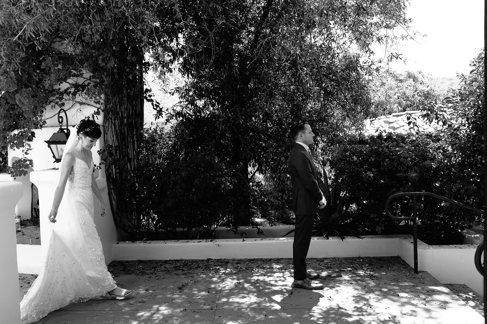 A black and white photo of a bride and groom standing apart, outdoors, with the groom looking at the bride as she walks away as they have their first look at their garden party wedding